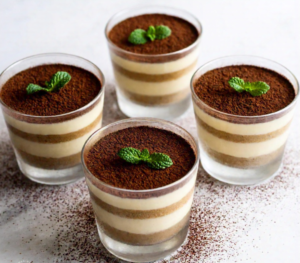 Individual servings of gluten free tiramisu in elegant glass cups, garnished with cocoa powder and fresh mint leaves.