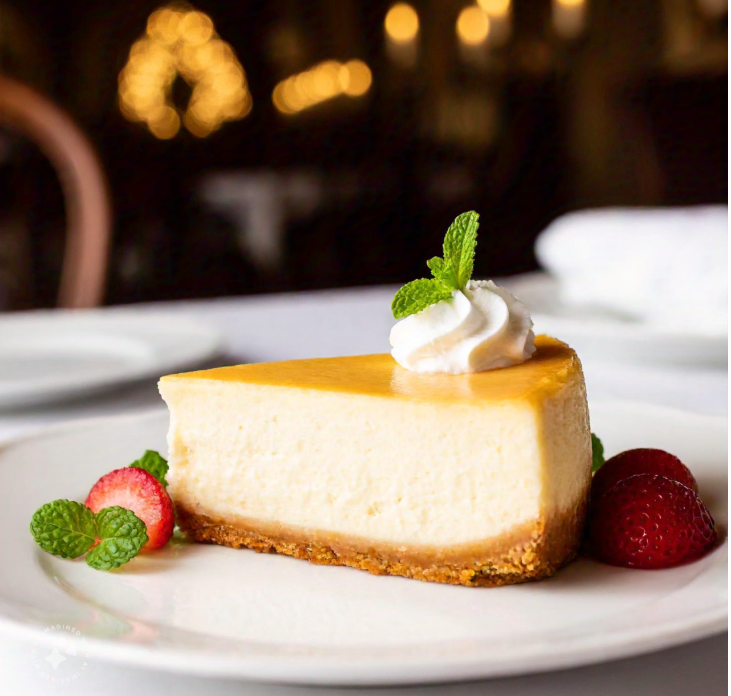 Slice of Biltmore Cheesecake with strawberries and mint, served on a white plate.