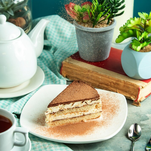 A slice of Costco tiramisu served on a plate with garnished cocoa and a sprig of mint.