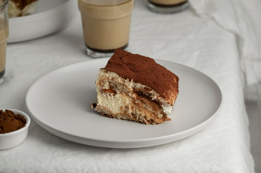 A single slice of alcohol-free tiramisu served on a white plate with a dusting of cocoa powder and a fork beside it.