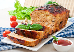 Perfectly smoked meatloaf on a wooden cutting board with a caramelized glaze, surrounded by fresh herbs and a smoking grill in the background.