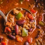 A bowl of Old Fashioned Chili topped with cheese and cilantro, served with crusty bread.